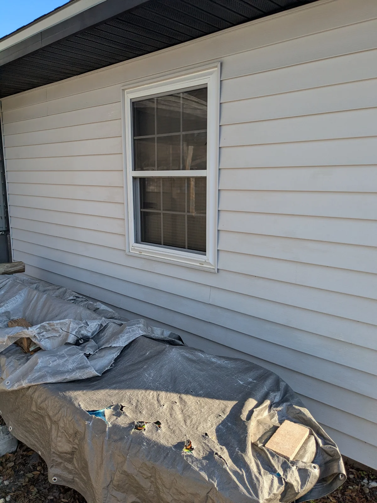 White siding house with covered items outside.