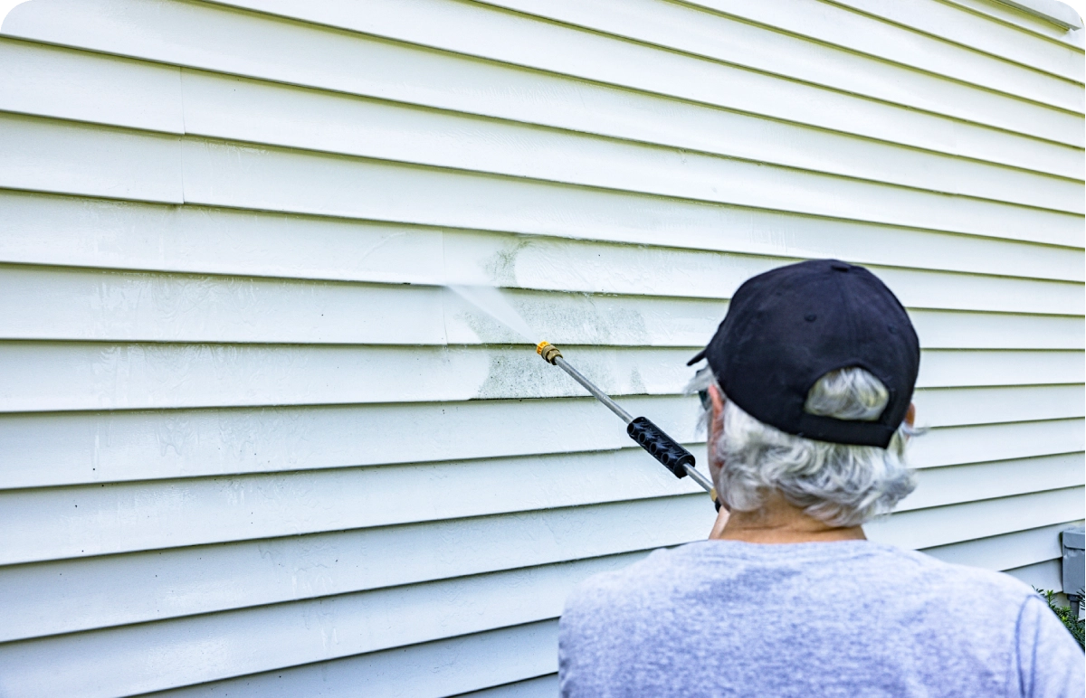 Person pressure washing house siding.
